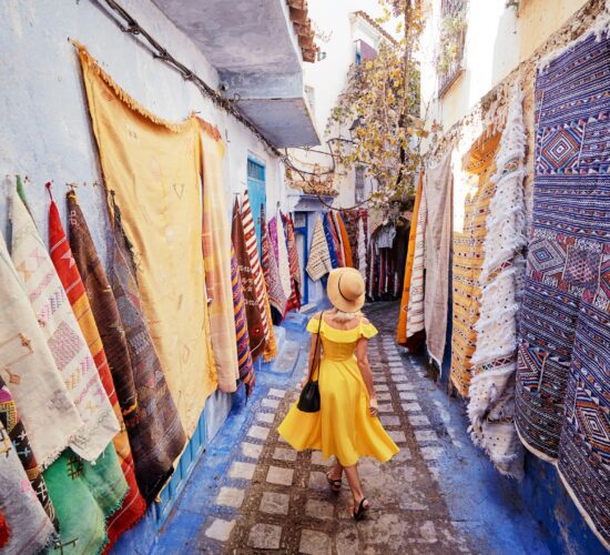 Colorful traveling by Morocco. Young woman in yellow dress walking in medina of blue city Chefchaouen.